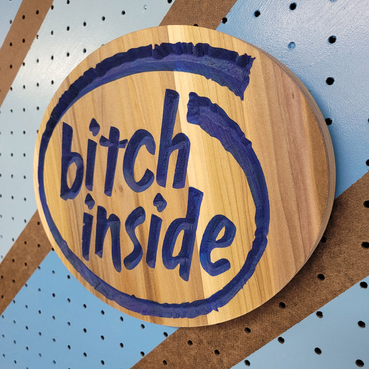 Angled shot of a Handcrafted relief-carved hardwood sign featuring a design inspired by the Intel logo, with the text "Bitch Inside."