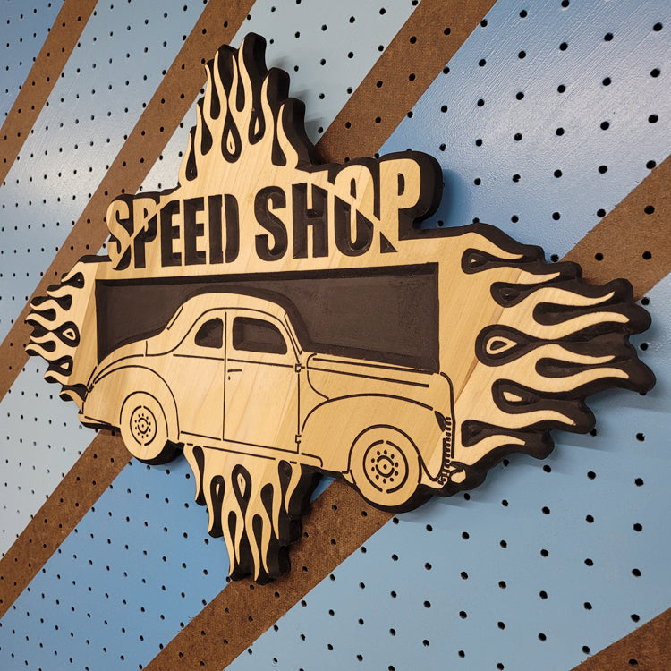 Angled shot of a custom hardwood Speed Shop garage sign with relief carved vintage hot rod and flame design on a striped pegboard