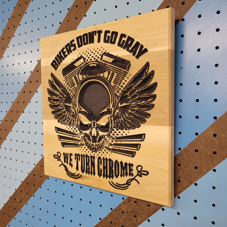 Angled shot of a relief carved hardwood sign featuring a winged skull with a motorcycle engine, Bikers Don't Go Gray, and We Turn Chrome text.