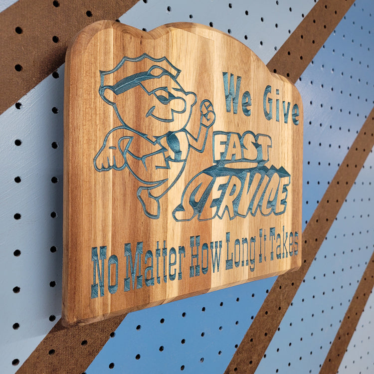 Angled shot of a relief carved hardwood sign featuring a cartoon mechanic and text: We Give Fast Service No Matter How Long It Takes.