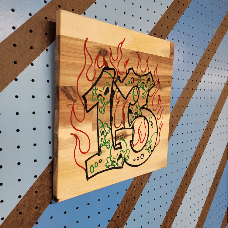 Angled shot of a Handcrafted relief-carved hardwood sign featuring the number "13" stylized with skulls and flames.