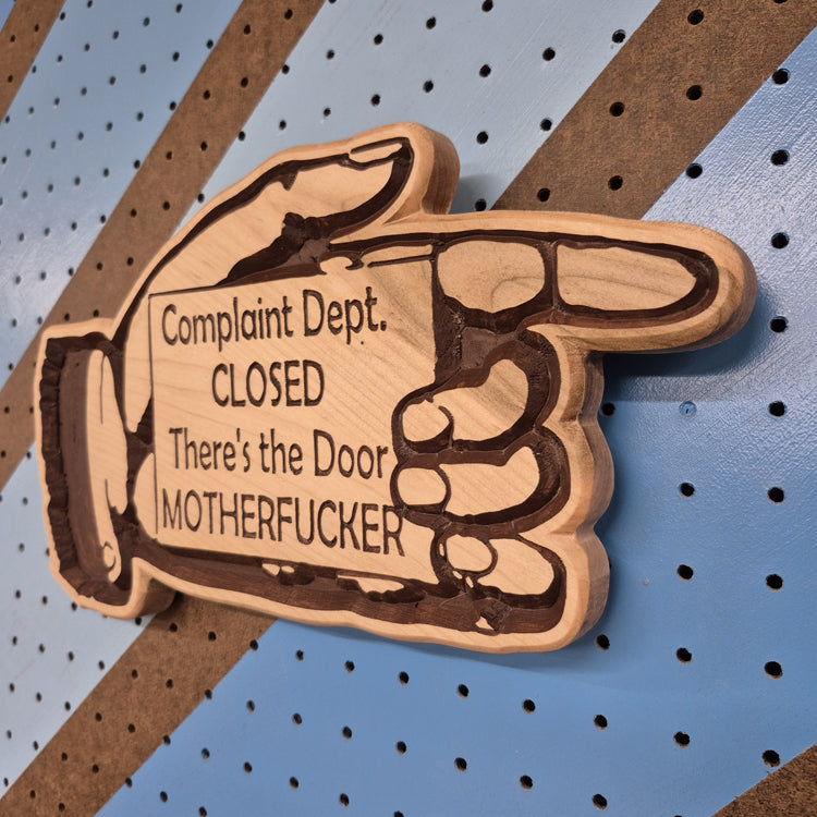 Angled shot of a Handcrafted relief-carved hardwood sign in the shape of a hand pointing, featuring the text "Complaint Dept. CLOSED There's the Door."