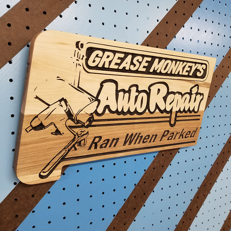 Angled shot of a Handcrafted relief-carved hardwood sign featuring the text "Grease Monkey's Auto Repair: Ran When Parked"