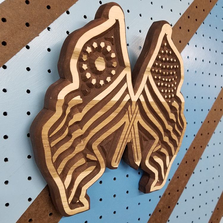 Angled shot of a Handcrafted relief-carved hardwood sign in the shape of crossed American flags.