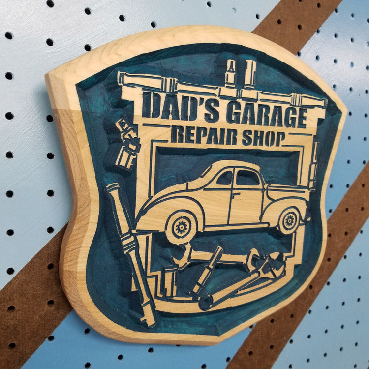 Angled shot of a Relief carved hardwood "Dad's Garage" sign featuring customizable vintage car art and tool motif.