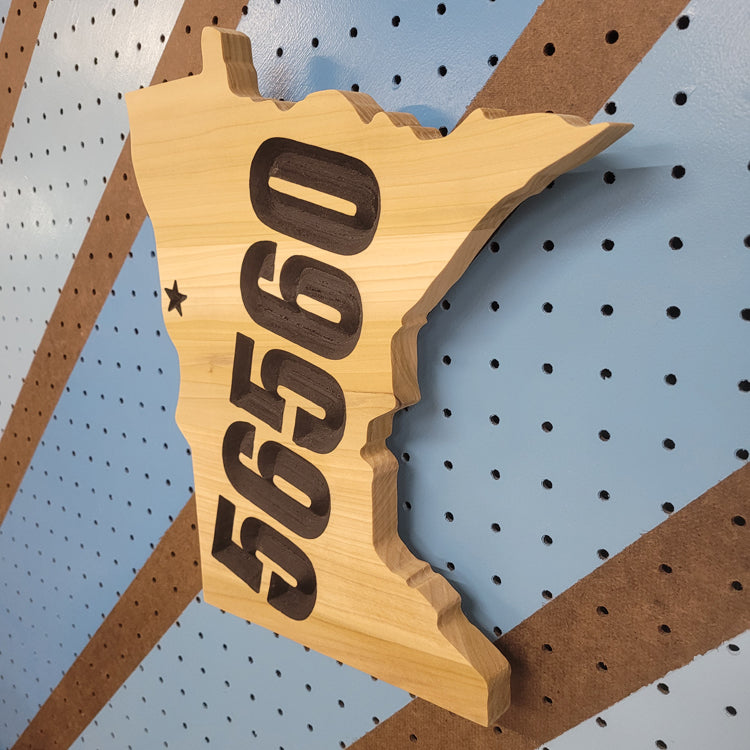 Angled shot of a Handcrafted relief-carved hardwood Minnesota sign featuring a customizable town name and zip code, allowing you to highlight your hometown with a personalized star placement.