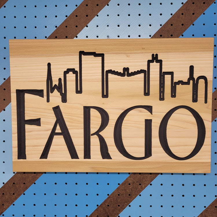 Relief carved hardwood sign featuring the iconic Fargo-Moorhead skyline silhouettes and Fraser-inspired lettering.