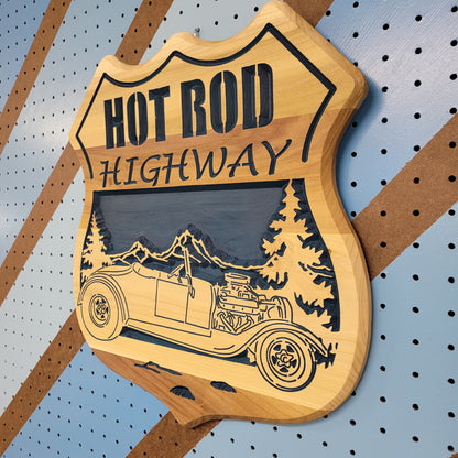 Angled shot of a fully customizable relief carved hardwood shield-shaped sign featuring a vintage hot rod convertible and pine trees.