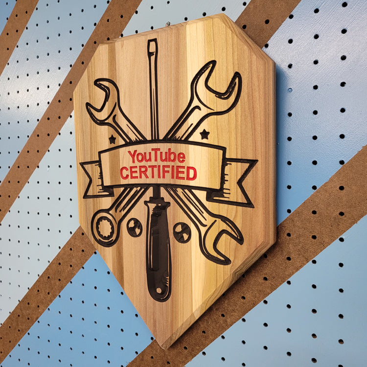 Angled shot of a custom hardwood wrench driver sign with YouTube Certified relief carving on a shop pegboard.