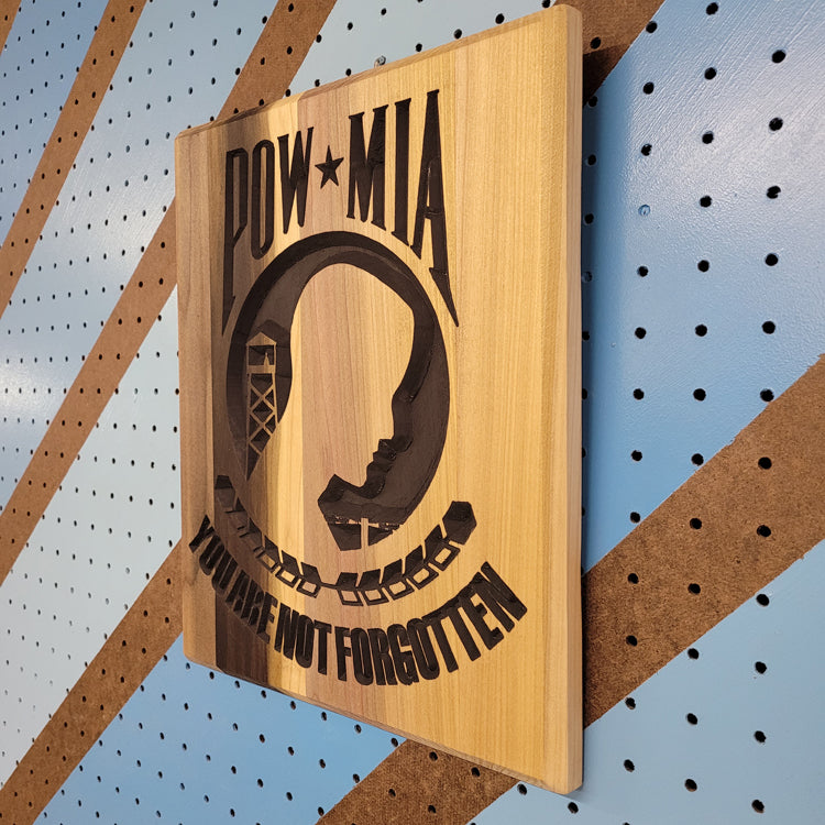 Angled shot of a relief carved hardwood POW MIA sign with a silhouette design and You Are Not Forgotten text on a striped pegboard.