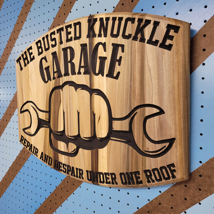 Angled shot of a Relief carved hardwood sign featuring the text: "The Busted Knuckle Garage: Repair and Despair Under One Roof."