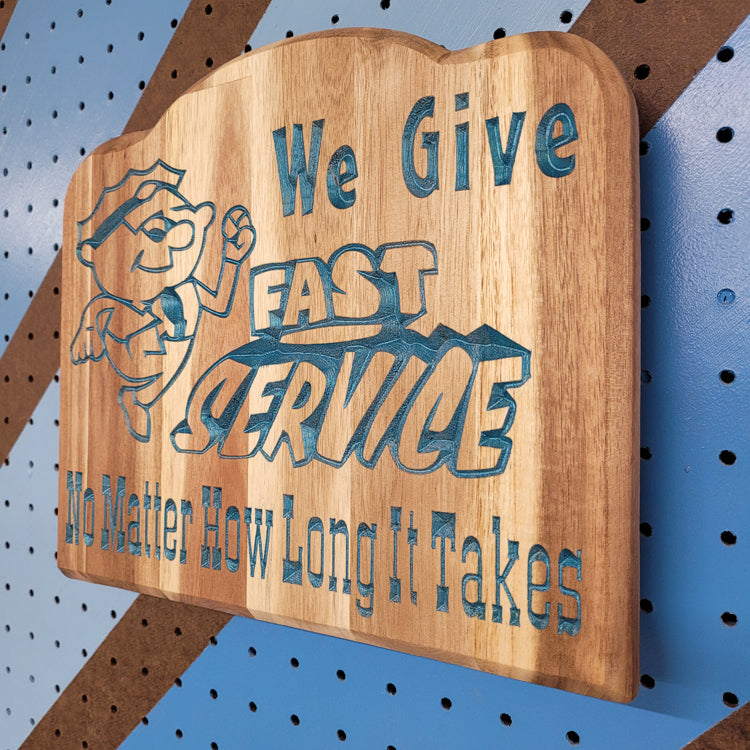 Angled shot of a relief carved hardwood sign featuring a cartoon mechanic and text: We Give Fast Service No Matter How Long It Takes.