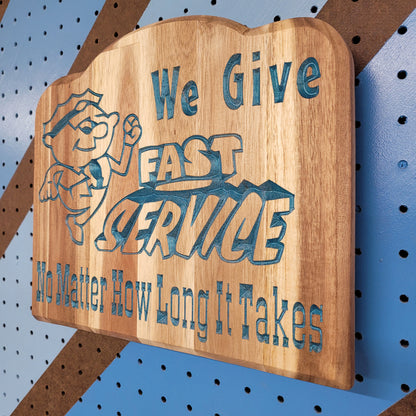 Angled shot of a relief carved hardwood sign featuring a cartoon mechanic and text: We Give Fast Service No Matter How Long It Takes.