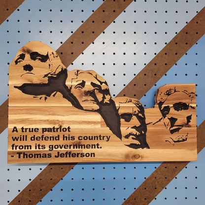 Relief carved hardwood Mount Rushmore sign with Thomas Jefferson quote on a striped pegboard.