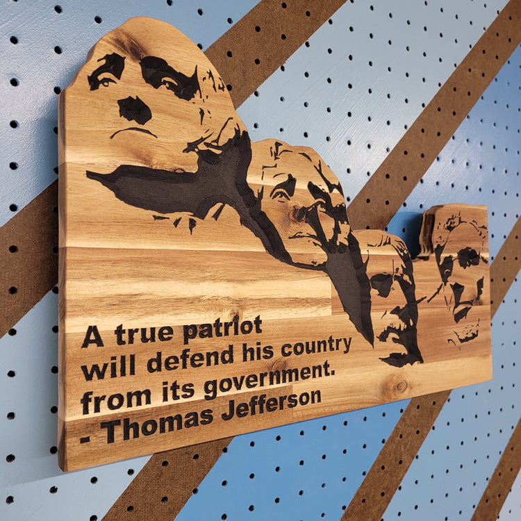 Angled shot of a relief carved hardwood Mount Rushmore sign with Thomas Jefferson quote on a striped pegboard.