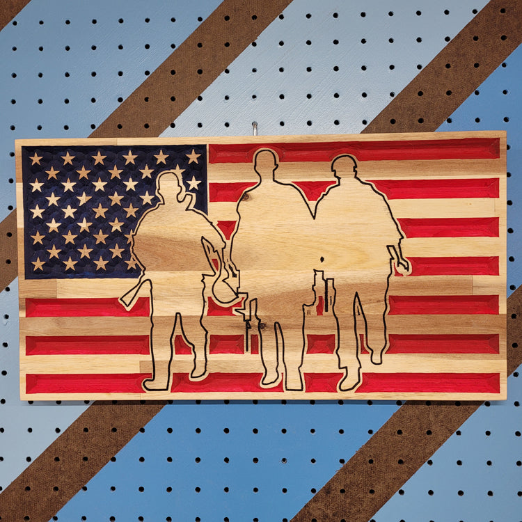 Relief carved hardwood American flag sign featuring a precision-cut silhouette of three soldiers on a pegboard.
