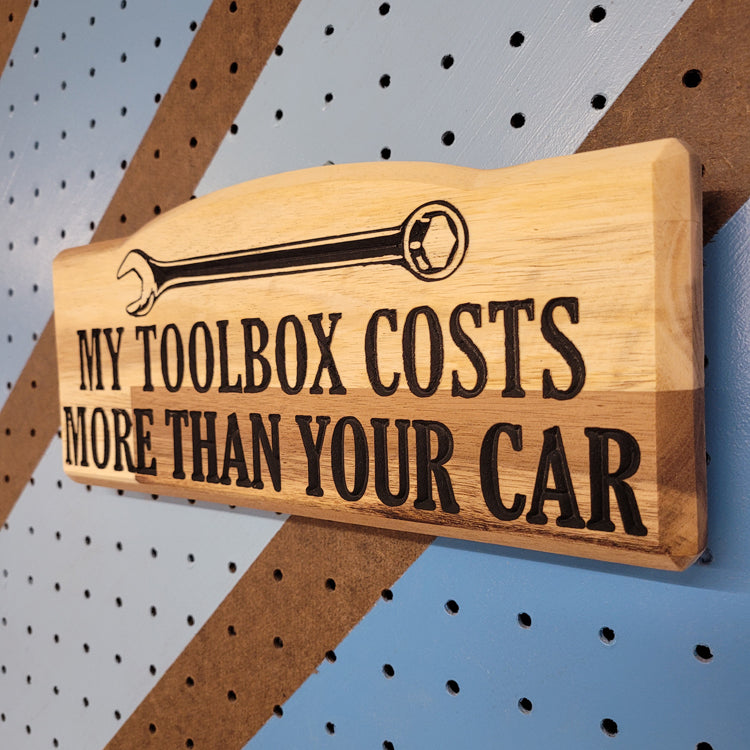 Angled shot of a custom hardwood novelty garage sign with carved wrench graphic and My Toolbox Costs More Than Your Car text.