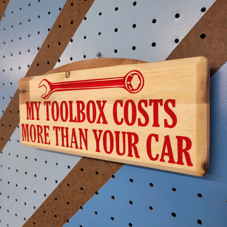 Angled shot of a custom hardwood novelty garage sign with carved wrench graphic and My Toolbox Costs More Than Your Car text.