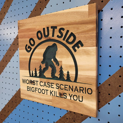 Angled shot of a Handcrafted relief-carved hardwood sign featuring a Bigfoot silhouette and the text "Go Outside, Worst Case Scenario Bigfoot Kills You."