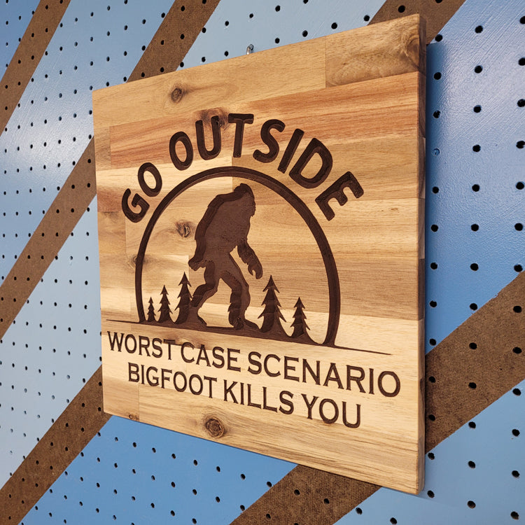 Angled shot of a Handcrafted relief-carved hardwood sign featuring a Bigfoot silhouette and the text "Go Outside, Worst Case Scenario Bigfoot Kills You."