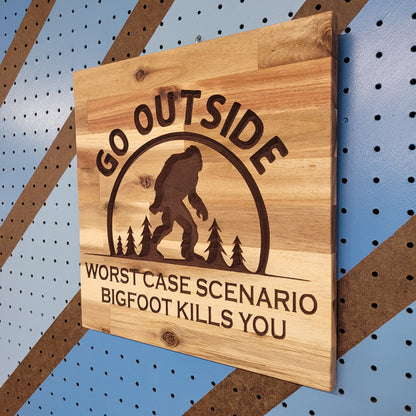 Angled shot of a Handcrafted relief-carved hardwood sign featuring a Bigfoot silhouette and the text "Go Outside, Worst Case Scenario Bigfoot Kills You."