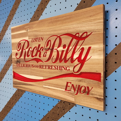 Angled shot of a relief carved hardwood sign with a classic red soda parody design and Rock-a-Billy text on a striped pegboard.