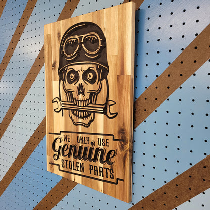 Angled shot of a custom hardwood garage sign with relief carved skull wearing a biker helmet and We Only Use Genuine Stolen Parts text.