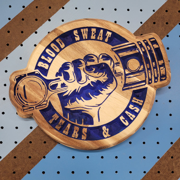 Relief carved hardwood sign with blue painted piston fist design and Blood Sweat Tears & Cash text on a striped pegboard.