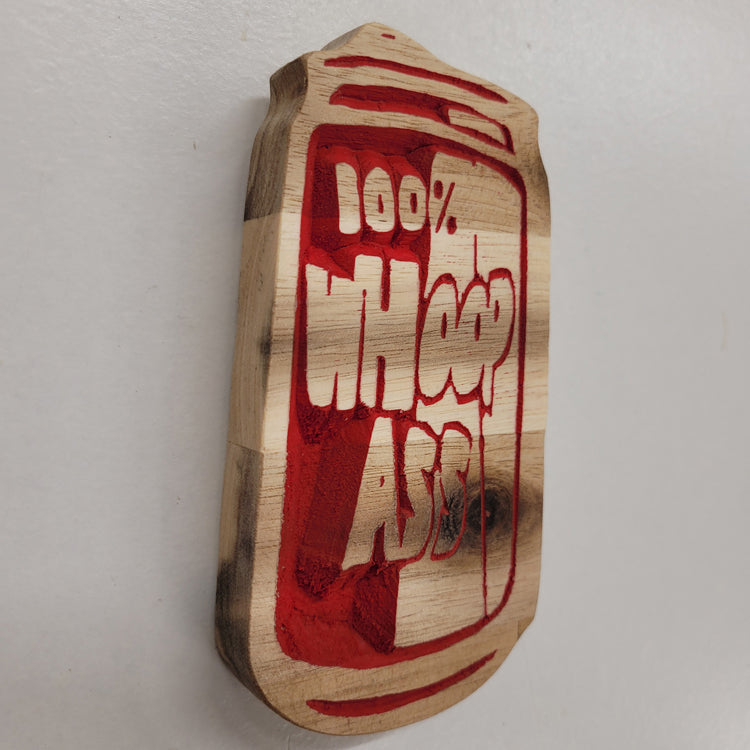 Angled shot of a custom hardwood sign carved into a soda can shape featuring a 100% Whoop Ass red relief design.