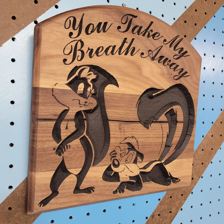 Angled shot of a Handcrafted relief-carved hardwood sign featuring a Pepe Le Pew and Penelope Pussycat inspired design with the text "You Take My Breath Away."