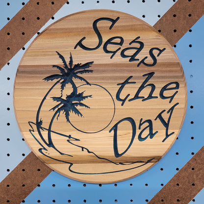 Custom circular hardwood sign with relief carved palm tree beach design and Seas the Day text on a striped pegboard.