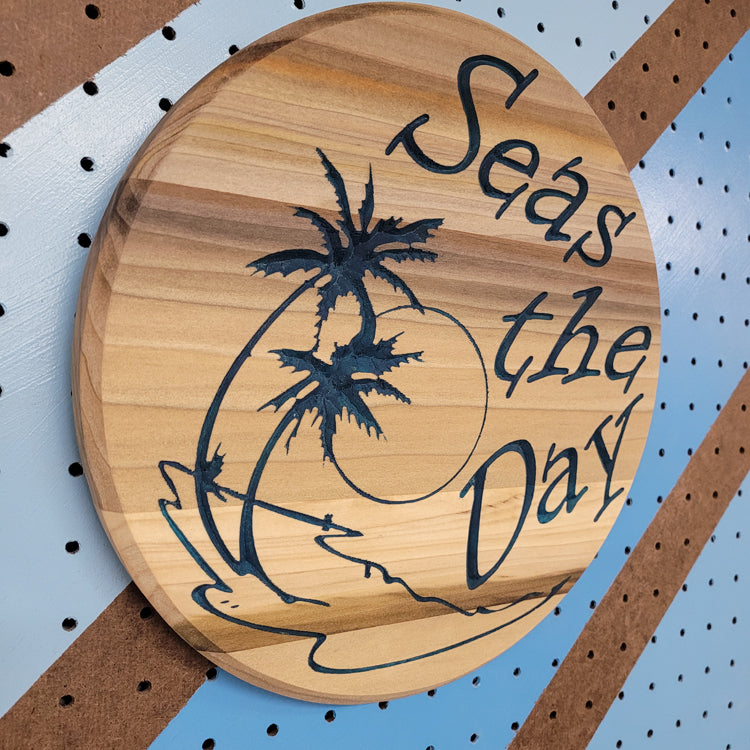 Angled shot of a custom circular hardwood sign with relief carved palm tree beach design and Seas the Day text.