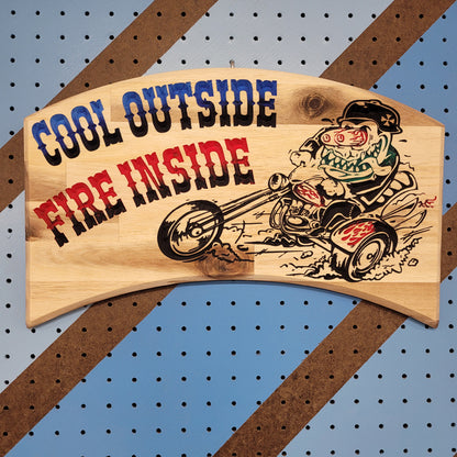 Relief carved hardwood sign with a retro monster chopper trike design and Cool Outside, Fire Inside text on a blue and brown striped pegboard.
