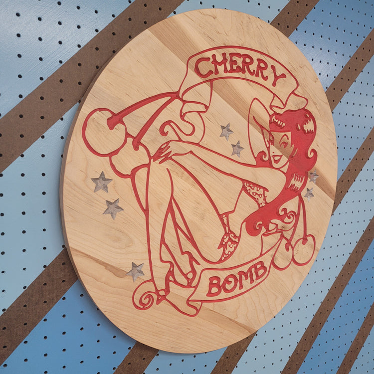 Angled shot of a Handcrafted relief-carved hardwood sign featuring a retro "Cherry Bomb" pinup design.
