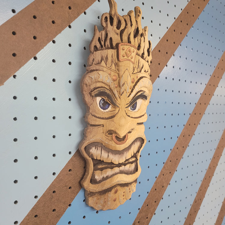 Angled shot of a 3D relief carved hardwood Tiki totem sign with unique hand-painted details on a blue pegboard.