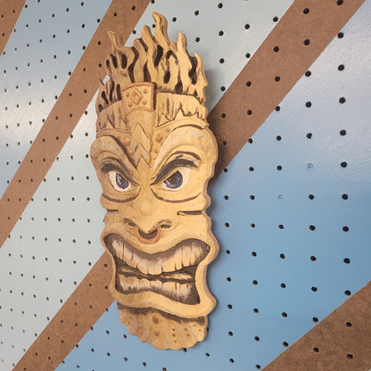 Angled shot of a 3D relief carved hardwood Tiki totem sign with unique hand-painted details on a blue pegboard.