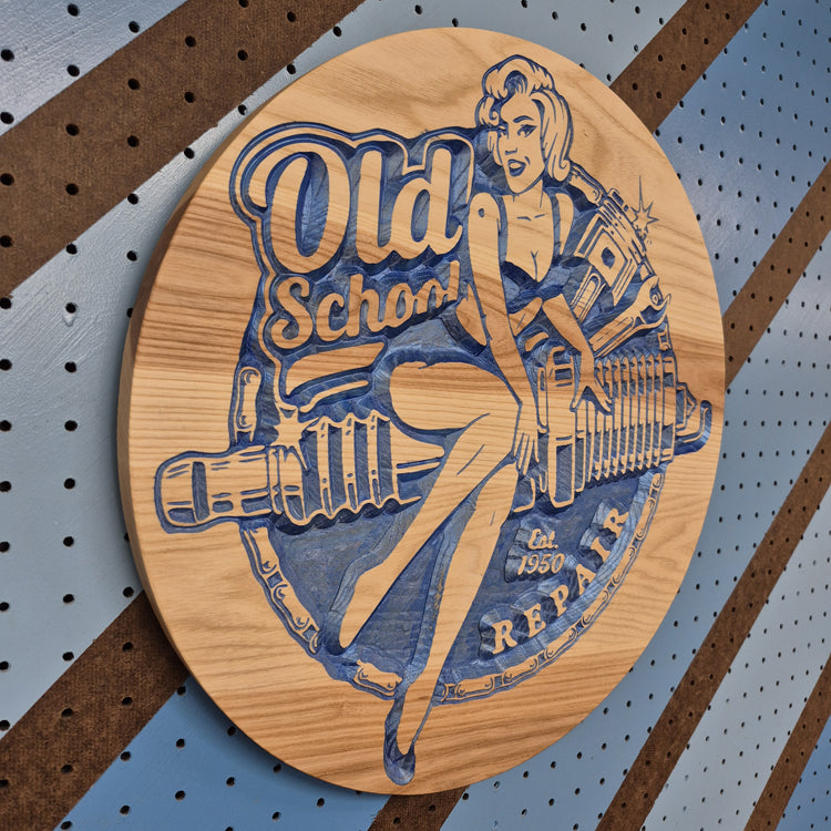 Angled shot of a relief carved hardwood sign with a retro pinup woman holding a wrench on a spark plug design with Old School Repair text.