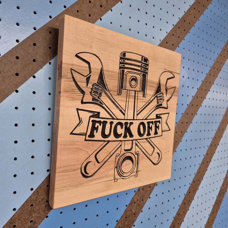 Angled shot of a relief carved hardwood sign featuring a piston and wrench design with the text: Fuck Off.