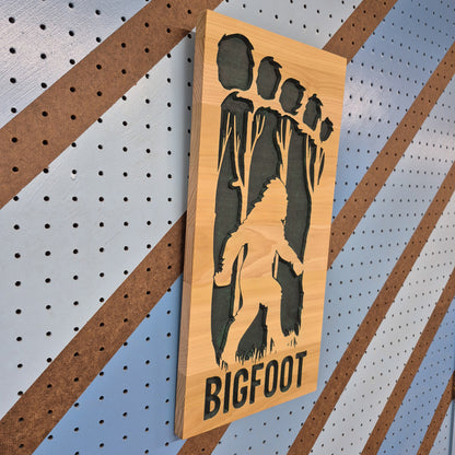 Angled shot of a Handcrafted relief-carved hardwood "Big Foot" silhouette sign, precision-cut and hand-finished for high-quality, cryptid-themed wall decor.