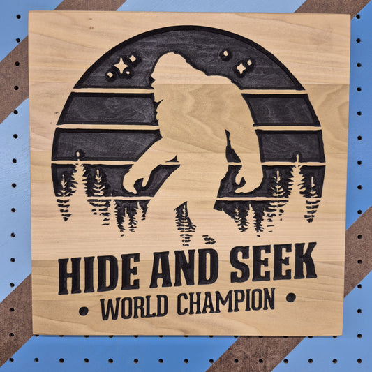 Handcrafted relief-carved hardwood sign featuring a Bigfoot silhouette and the text "HIDE AND SEEK WORLD CHAMPION."