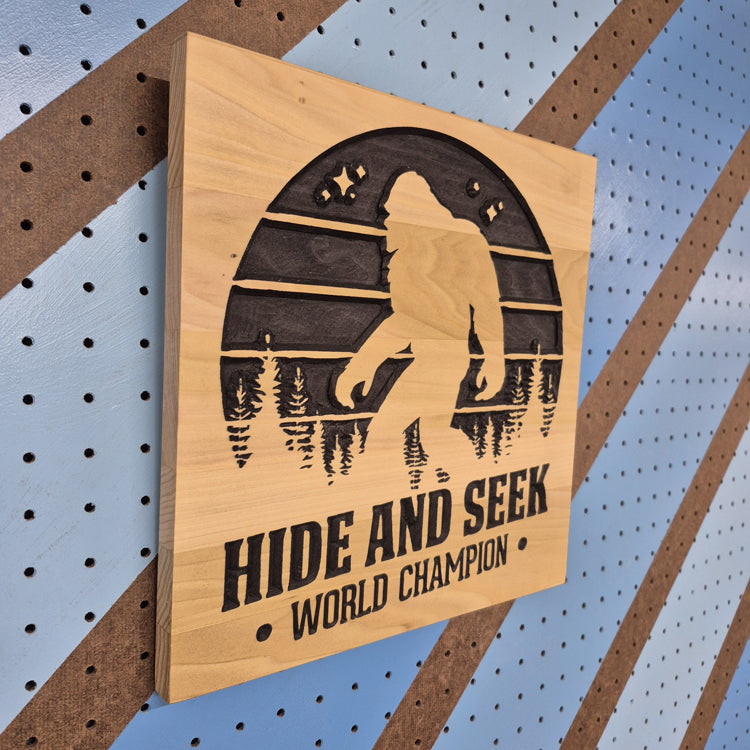 Angled shot of a Handcrafted relief-carved hardwood sign featuring a Bigfoot silhouette and the text "HIDE AND SEEK WORLD CHAMPION."