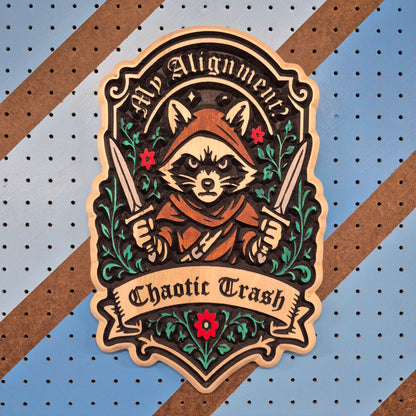 A vertical solid hardwood carved sign featuring a detailed fantasy raccoon character wearing a hooded cloak and holding twin daggers. The banner text reads "Chaotic Trash" below a circular frame with the words "My Alignment Is".