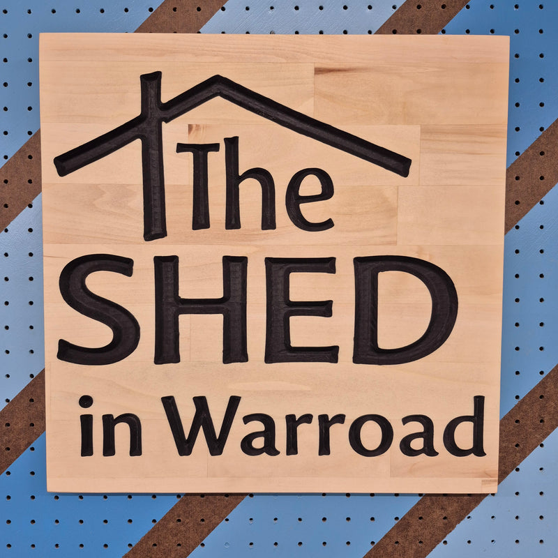 Custom CNC-carved wooden sign featuring a stylized house roof outline and the text 'The SHED in Warroad'
