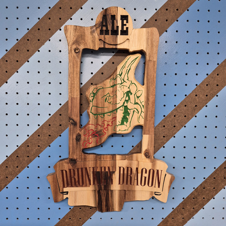 A vertical solid hardwood carved sign for "The Drunken Dragon Pub". The detailed design features a whimsical dragon wrapped around a massive, overflowing mug of beer, displayed against a blue and orange diagonal patterned background.