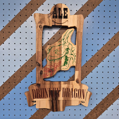 A vertical solid hardwood carved sign for "The Drunken Dragon Pub". The detailed design features a whimsical dragon wrapped around a massive, overflowing mug of beer, displayed against a blue and orange diagonal patterned background.