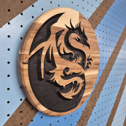 An angled side shot of the circular Yin Dragon wooden plaque, highlighting the dimensional depth of the CNC relief cuts and the contrast of the hand-painted black accents against a striped pegboard wall.