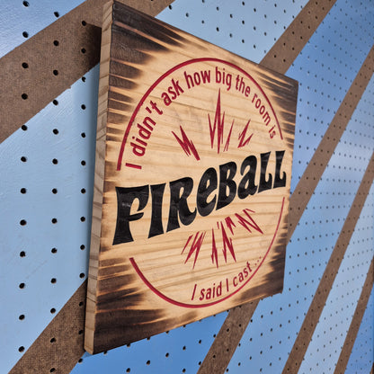 An angled side shot of the square Fireball quote wooden plaque, showcasing the clean, dimensional depth of the CNC relief cuts and the rich patterns of the natural hardwood grain against a striped pegboard wall.