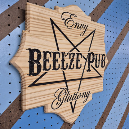 An angled side shot of the custom carved Beelze Pub wooden plaque, showcasing the deep dimensional relief of the CNC cuts and the rich patterns of the natural hardwood grain against a striped pegboard wall.