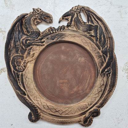 A top-down view of a circular solid hardwood dice rolling tray featuring a detailed 3D carving of two dragons around the border and a brown flocked velvet center, set against a light background.