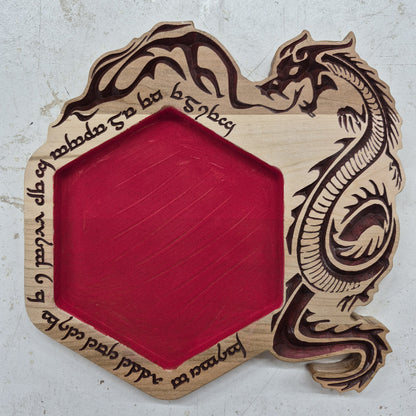 A top-down view of a hexagonal 10.5 by 10.5 inch solid hardwood dice rolling tray featuring a carved border with a dragon and fantasy runes, crisp hand-painted dark brown accents, and a red flocked velvet center.